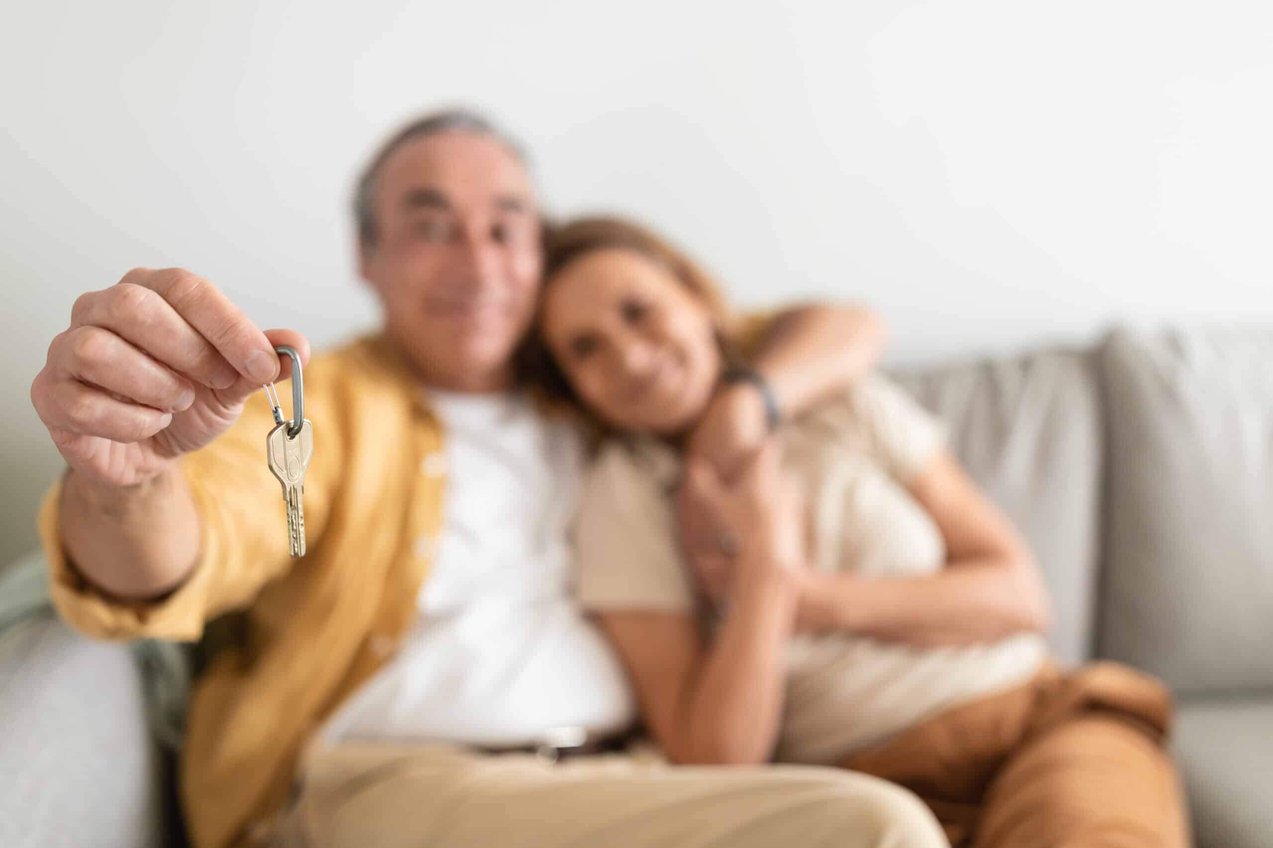 Real estate concept. Senior couple holding home keys, embracing, celebrating buying property